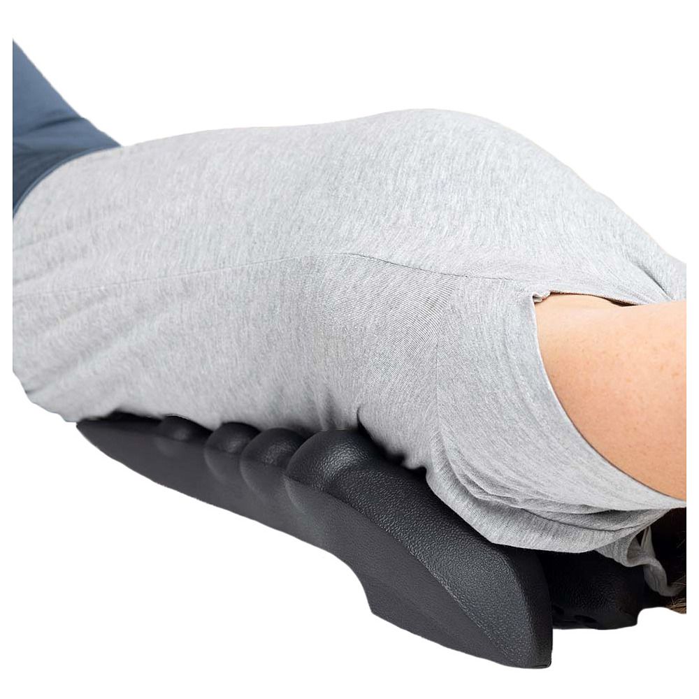 Person liegt auf dem Bauch. Ein schwarzes Massagegerät mit Noppen ist unter dem Bauch platziert. Person trägt ein graues T-Shirt.