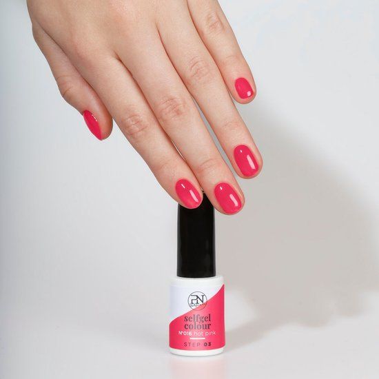 Hand mit lackierten Nägeln in N16 Hot Pink. Flasche PN Selfgel Vernis Semi-Permanent daneben.