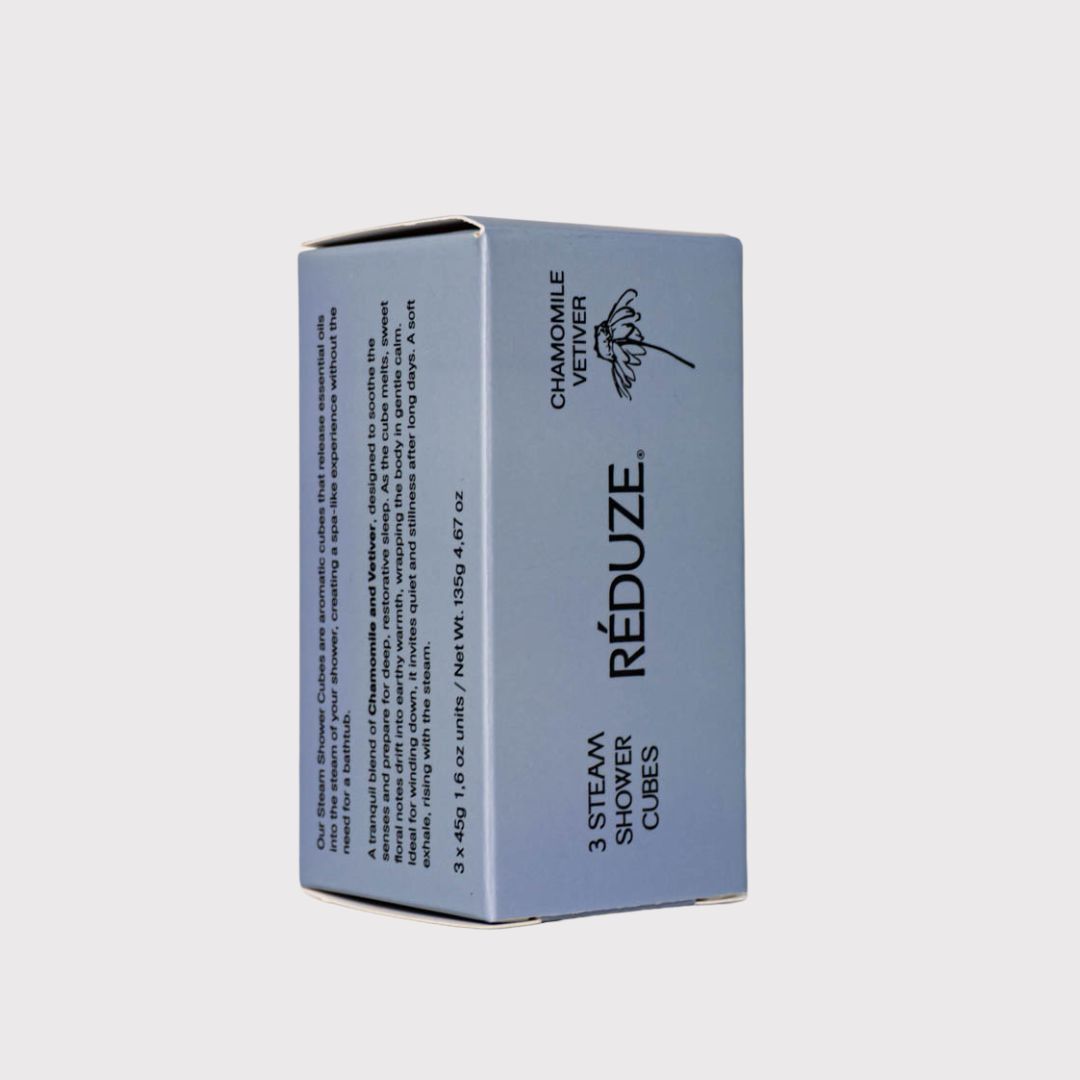 Eine blaue Schachtel mit RÉDUZE, Kamille & Vetiver und 3 Steam Shower Cubes. Eckige Form.