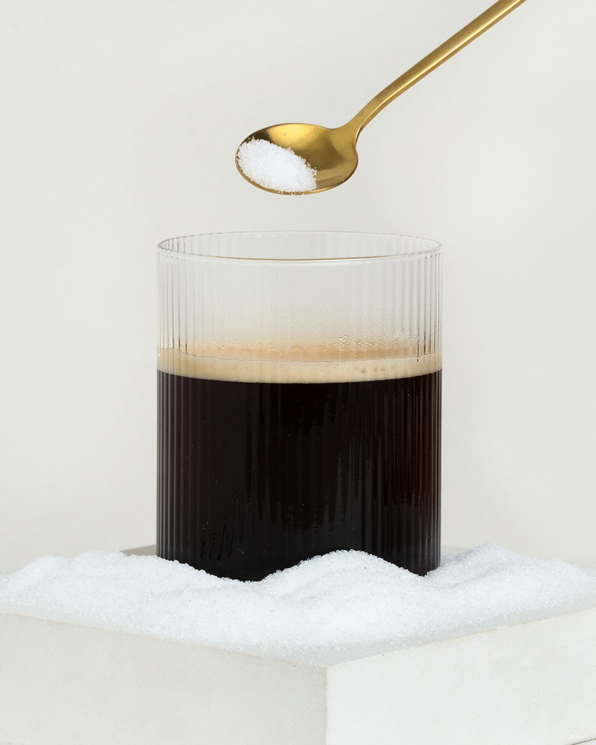 Ein Löffel mit Süßstoffpulver über einem Glas Kaffee, umgeben von Streusüße.