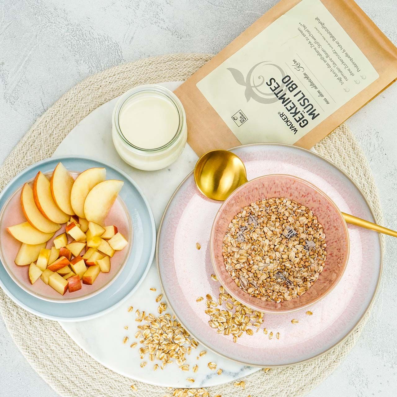 Gekeimtes Müsli Bio in Schale, Apfelstücke, Joghurtglas, goldener Löffel. Aufschrift: Wacker, Gekeimtes Müsli Bio.