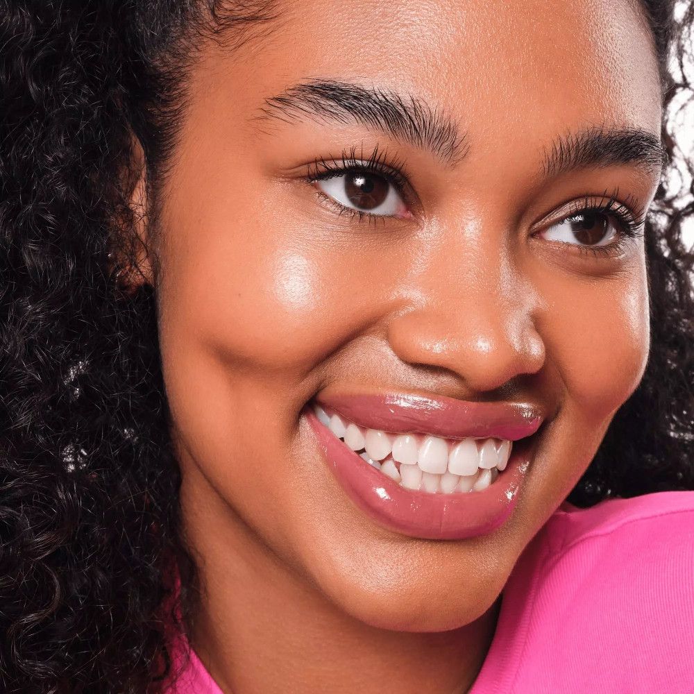 Porträt einer Frau mit rosafarbenem Lipgloss. Sie lächelt. Der Lipgloss ist glänzend und betont die Lippen. Haut glänzt.