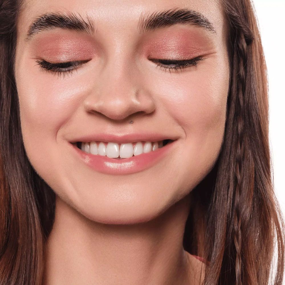 Porträt einer lächelnden Frau. Geschlossene Augen, rosa Lidschatten. Lange, braune Haare.