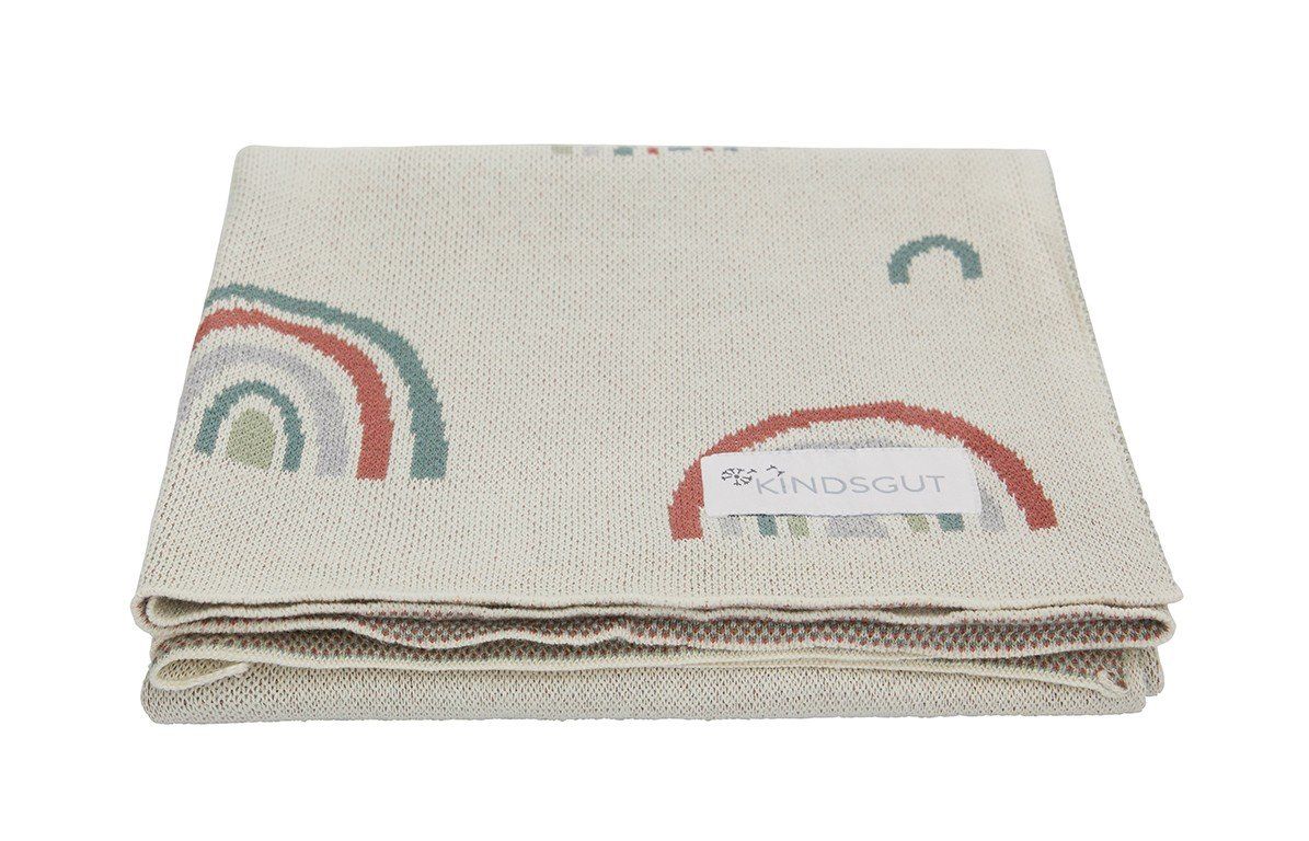 Gefaltete Decke mit Regenbogenmuster und Logo. Beige mit bunten Regenbogenmotiven. Das Logo ist sichtbar.