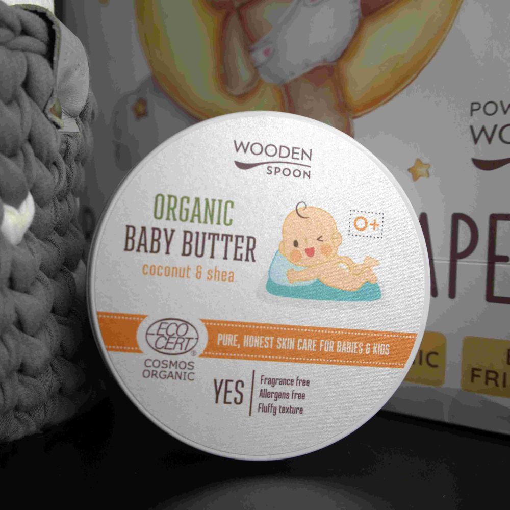 Dose "Wooden Spoon Organic Baby Butter" mit Baby-Illustration und Öko-Zertifizierung. Teilweise unscharf.