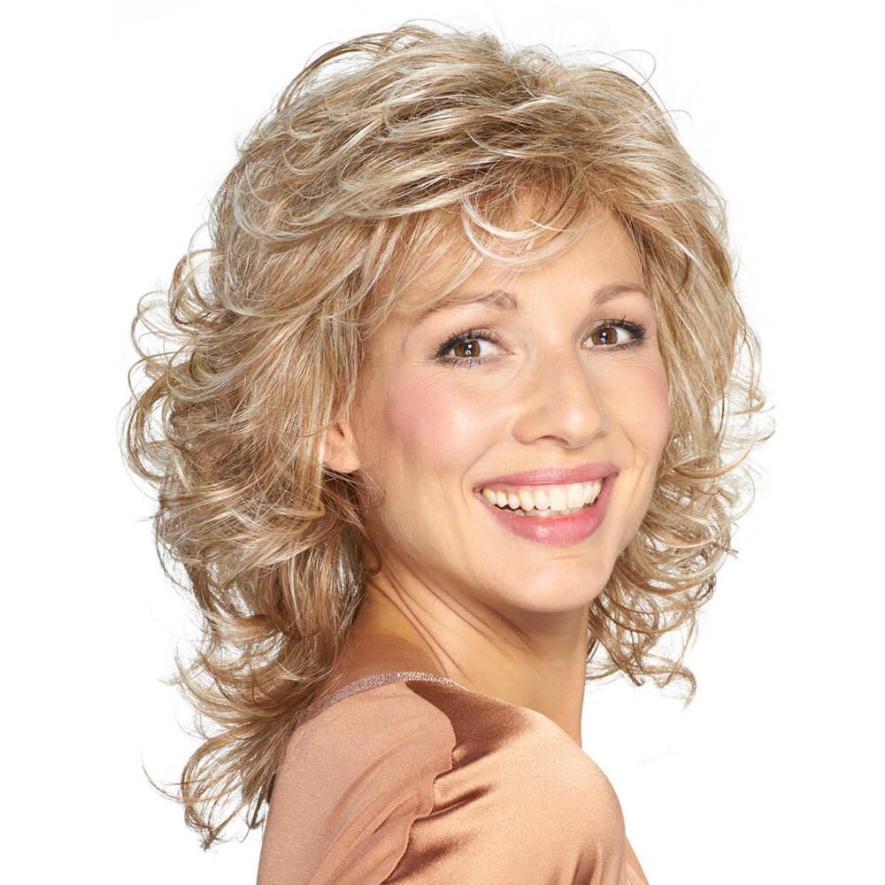 Frau mit blond gelockter Perücke, Blick zur Seite. Die Perücke hat einen Pony und ist leicht gestuft. Sie trägt ein helles Oberteil.