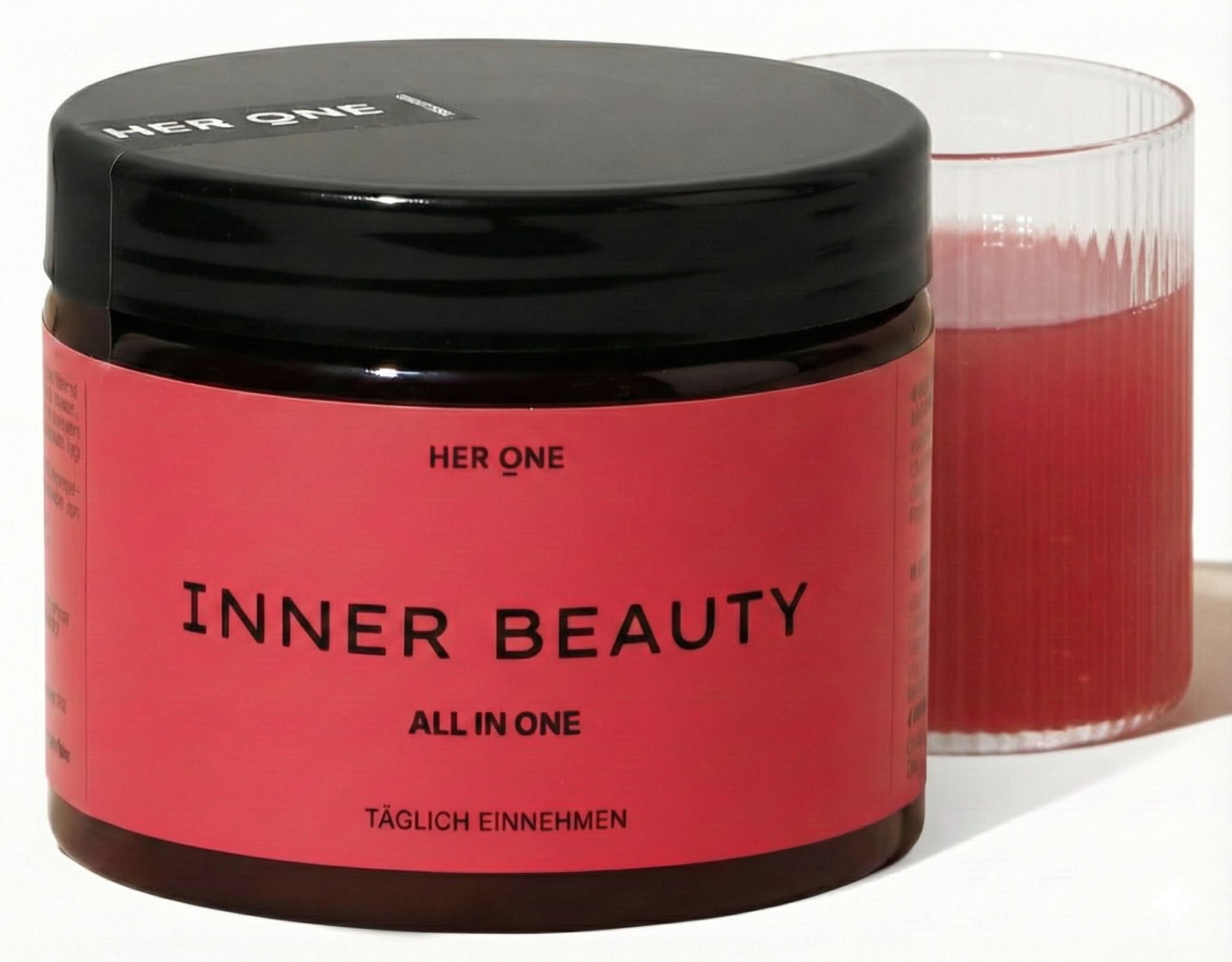 Rotes Glas mit schwarzem Deckel. Text: HER ONE INNER BEAUTY ALL IN ONE. Daneben ein Glas mit roter Flüssigkeit.