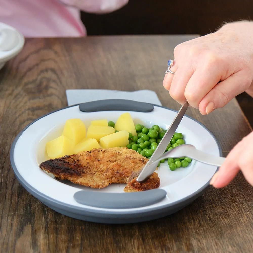 Teller mit Essen. Person schneidet Fleisch mit Messer und Gabel.