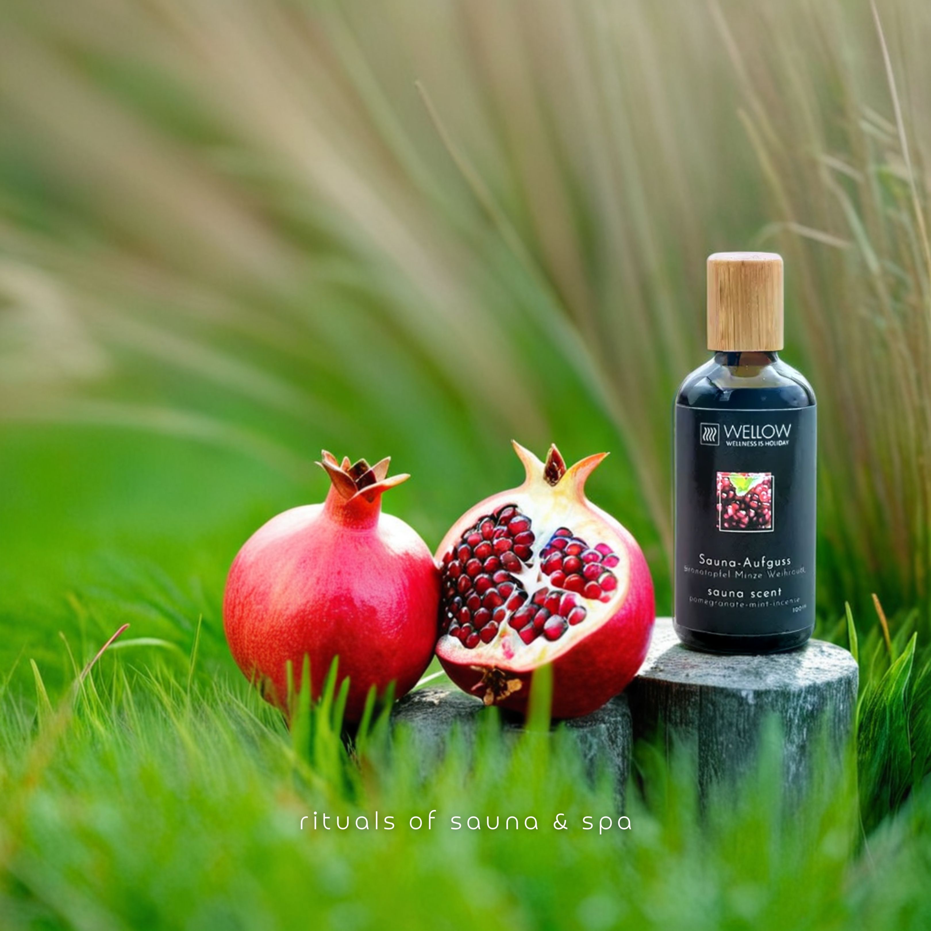 Granatäpfel auf einem Baumstumpf. Eine Frucht ist halbiert. Daneben eine Flasche mit Holzverschluss und Etikett. Sauna-Aufguss Granatapfel-Minze-Weihrauch.