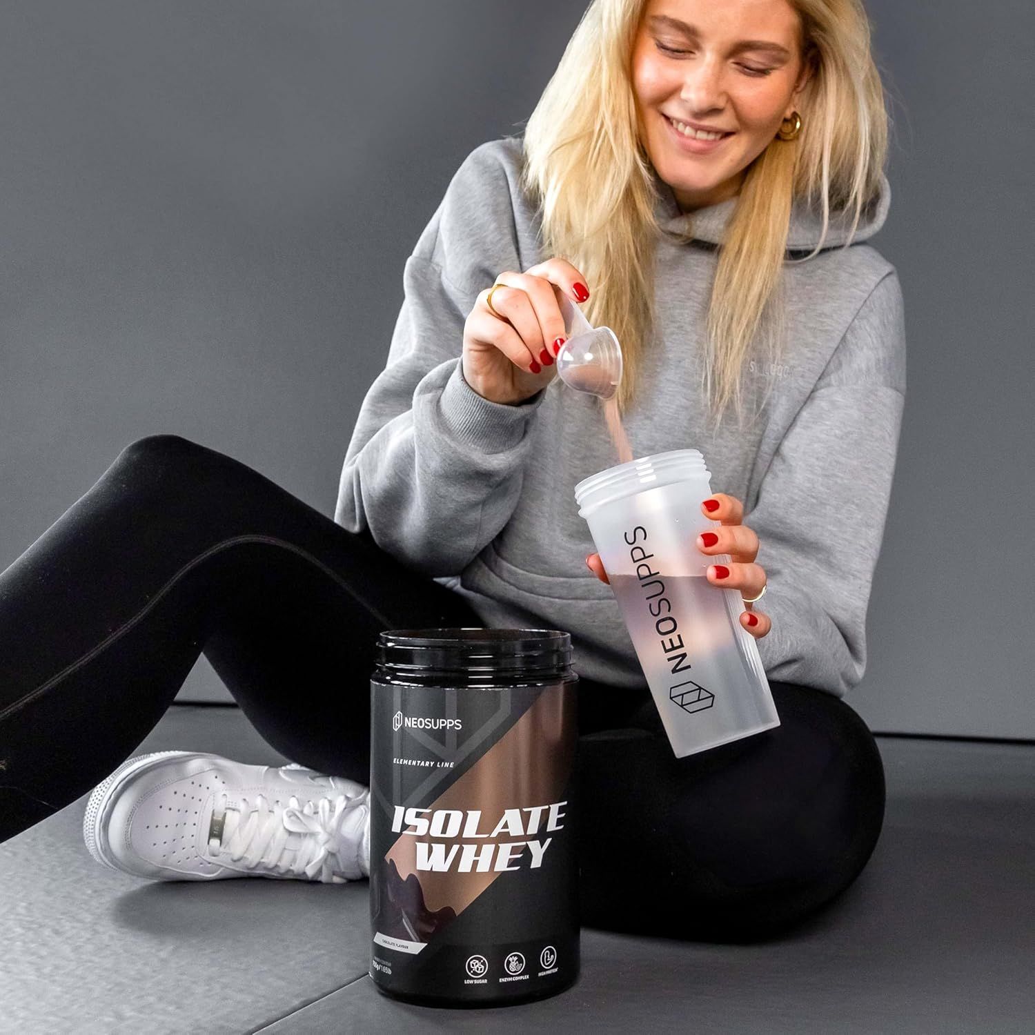 Frau mischt Isolate Whey in einem Shaker. Dose und Shaker mit Logo. Pulver wird in den Shaker gegeben.