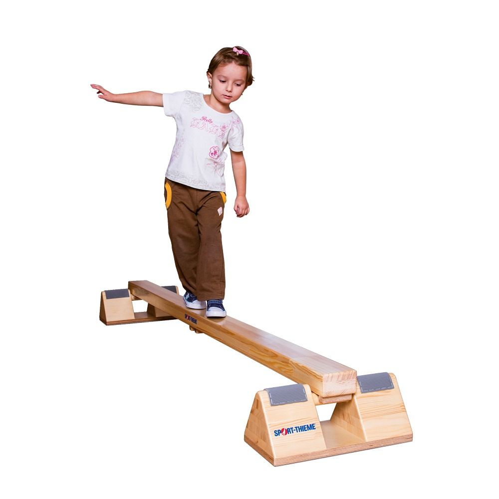 Ein Kind balanciert auf einem Holz-Balancierbalken. Der Balken hat Holzfüße und ist mit dem Schriftzug Sport-Thieme versehen.