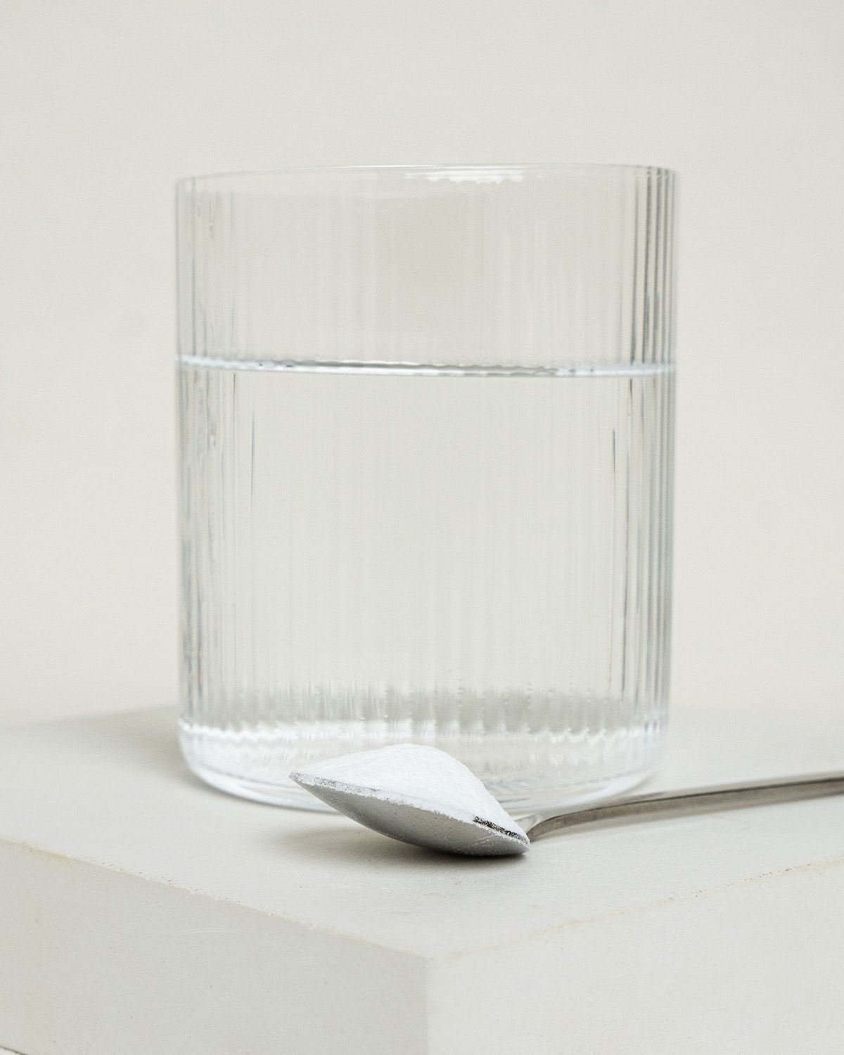 Ein Löffel mit weißem Pulver neben einem Glas Wasser mit Rillen.