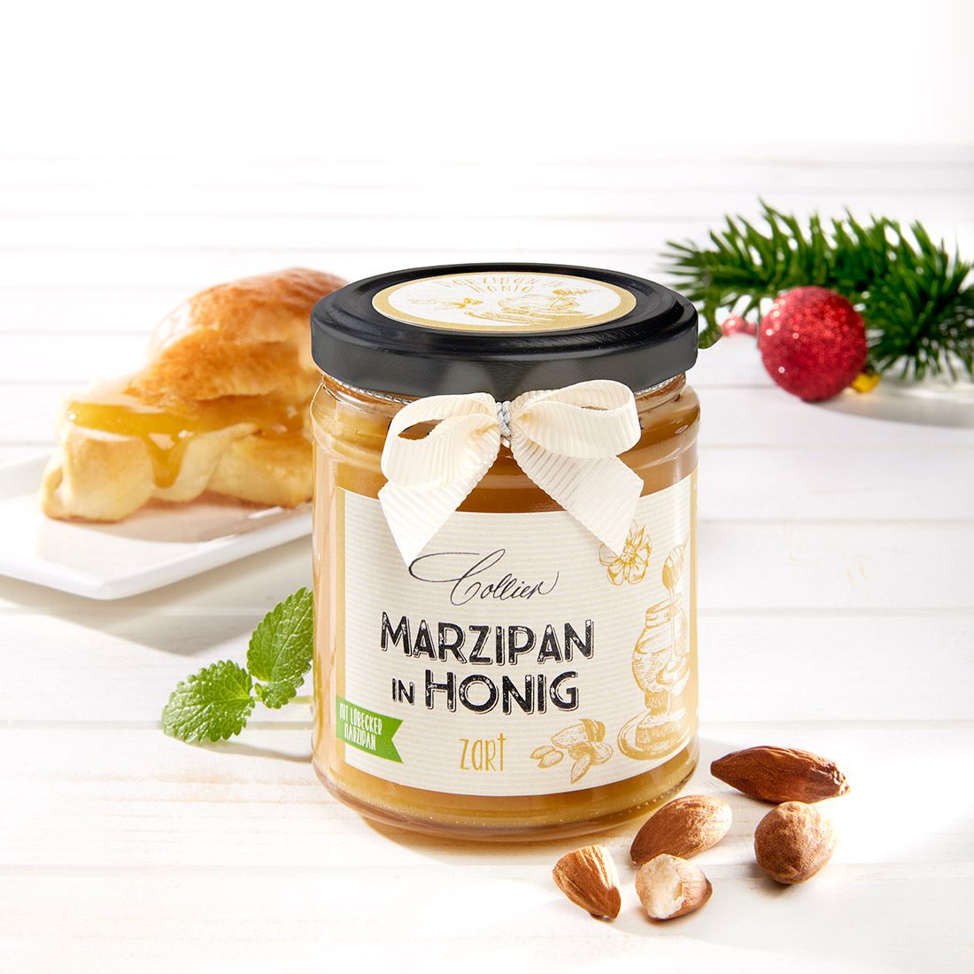 Glas Marzipan in Honig, Etikett, schwarzer Deckel, Schleife. Schriftzug: Marzipan in Honig. Zart. Croissant, Mandeln, Tannenzweig, rote Kugel.