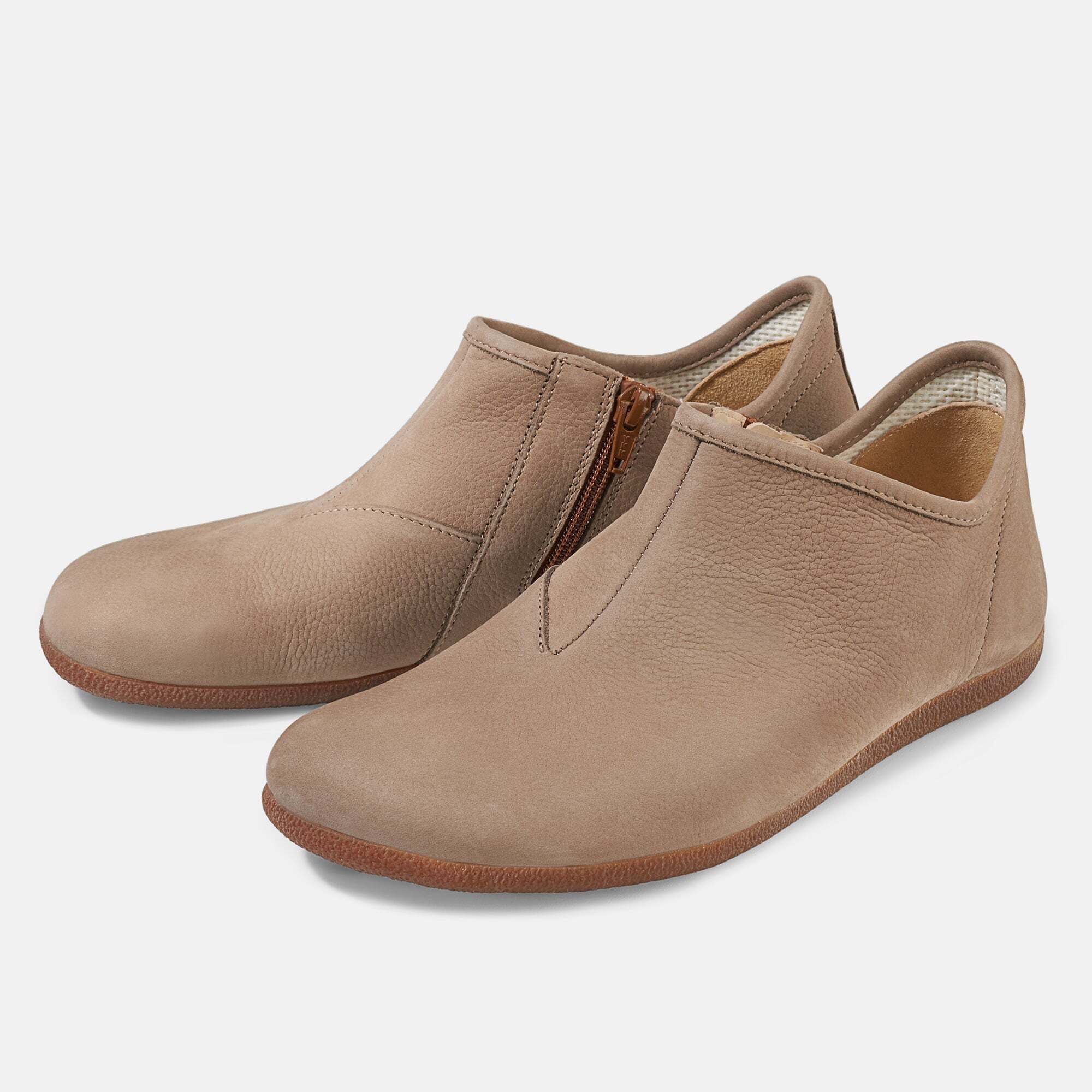 Beige Slipper mit seitlichem Reißverschluss. Flache Sohle, breite Passform. Zwei Schuhe nebeneinander, leicht schräg gestellt.