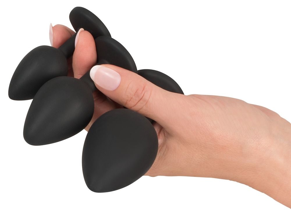 Hand hält eine Auswahl von schwarzen Anal-Plugs. Verschiedene Größen und Formen.