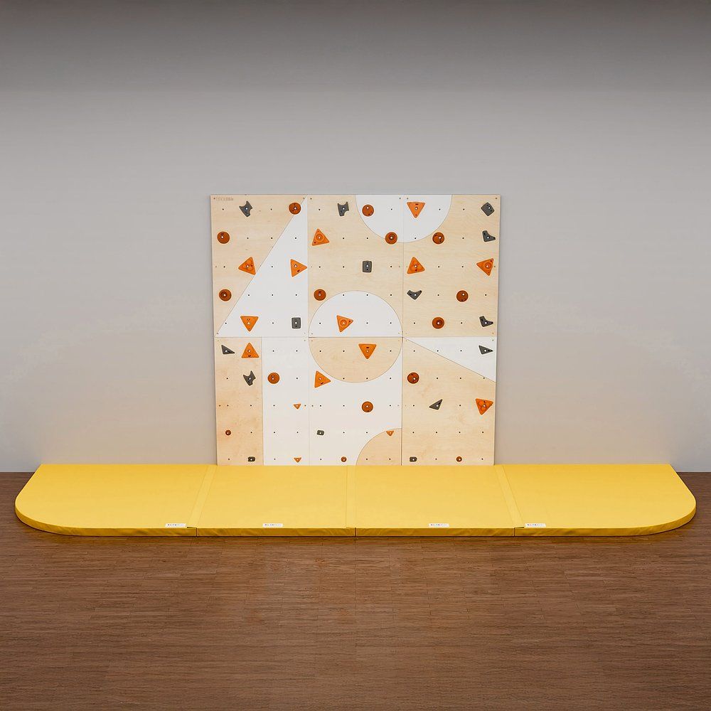 Kletterwand mit orangefarbenen und grauen Griffen. Gelbe Matte darunter.