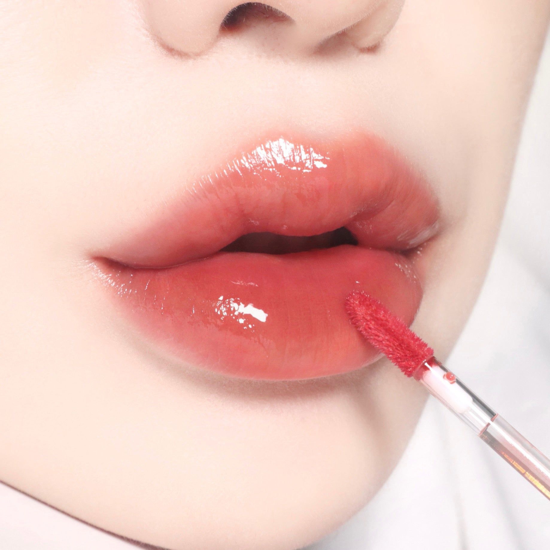 Nahaufnahme von Lippen mit glänzendem Lipgloss. Applikator in Gebrauch.