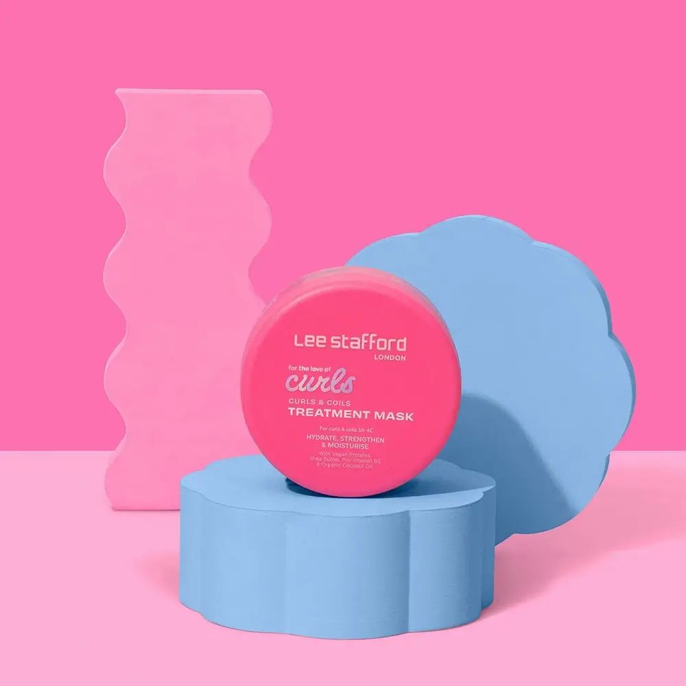 Runder rosa Tiegel mit Aufschrift 'Lee stafford', 'for the love of curls', 'CURLS & COILS TREATMENT MASK'. Auf blauem Podest.