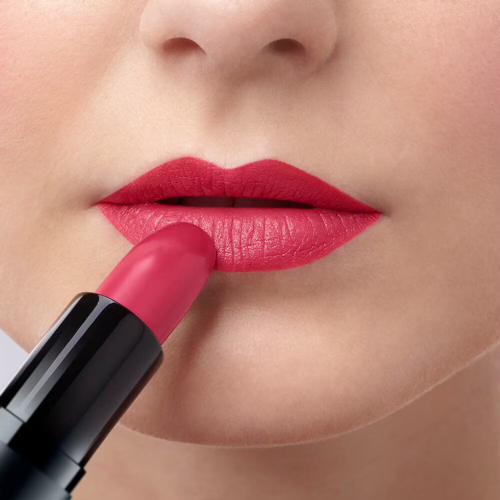 Person trägt rosafarbenen Lippenstift auf den Lippen auf. Schwarzer Lippenstift-Halter sichtbar.