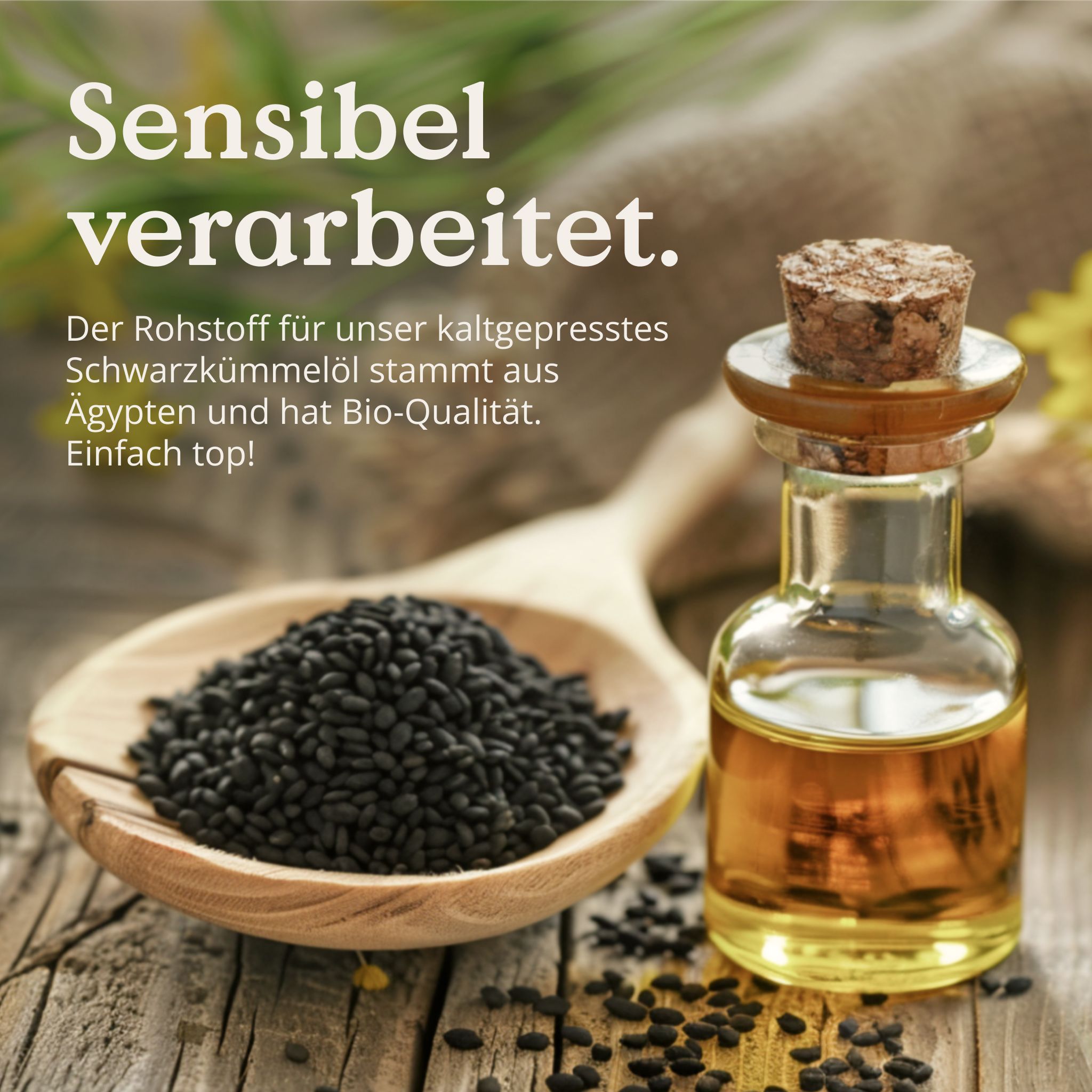 Glasflasche mit Korken und Schwarzkümmelöl, daneben Schwarzkümmelsamen auf Holzlöffel. Text: Sensibel verarbeitet.