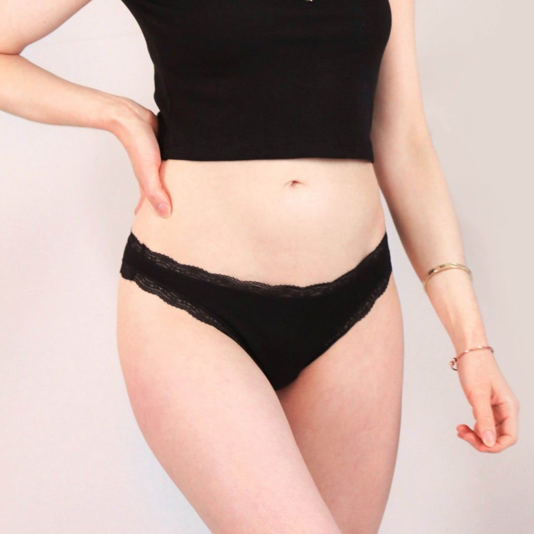Schwarzer Brazilian Slip mit Spitze. Model trägt Unterwäsche. Nahaufnahme.