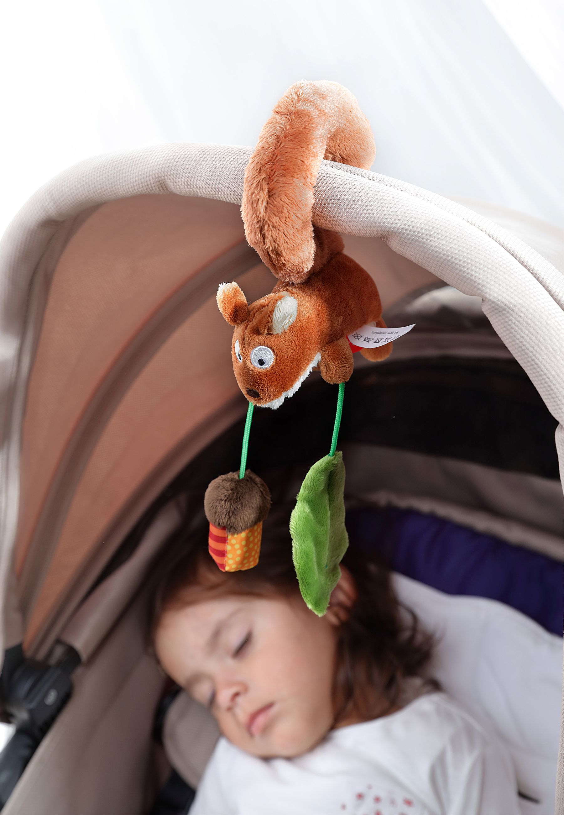 Plüsch-Eichhörnchen-Anhänger an Kinderwagen befestigt, neben schlafendem Baby.