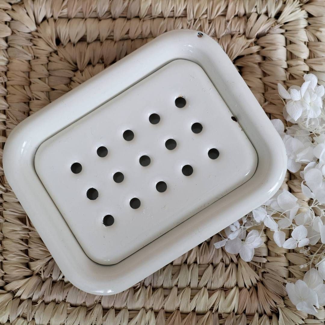 Porte-savon émaillé crème, rectangulaire avec trous. Placé sur un tressage, avec des fleurs blanches.