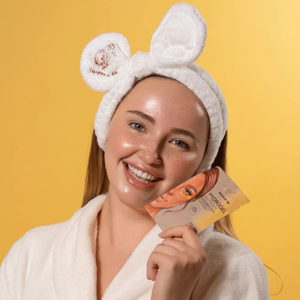 Femme tenant un paquet de coussinets pour les yeux. Inscription: Hydrogel. Elle porte un bandeau blanc et un peignoir. Fond jaune.
