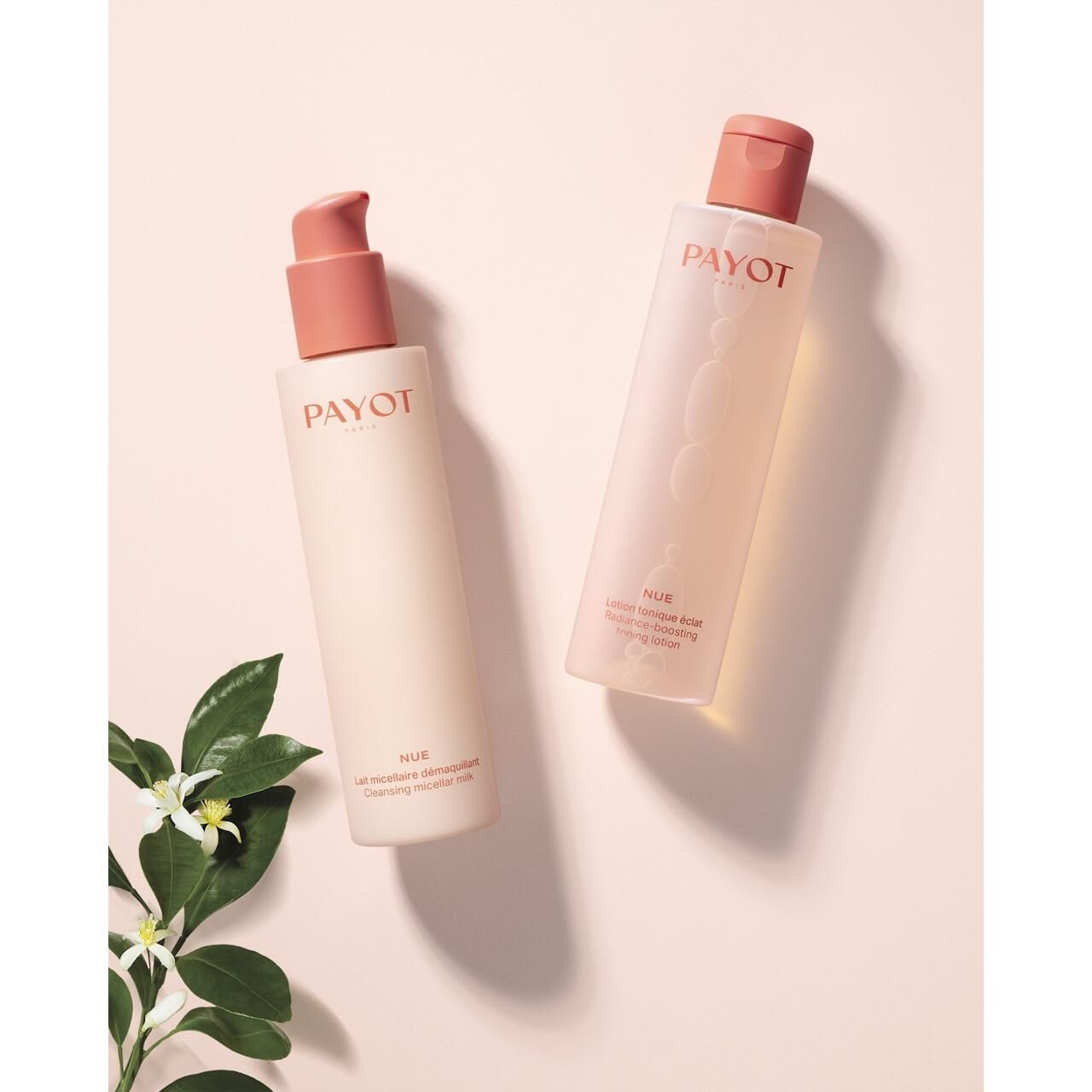 Zwei Payot Nue Lotion Tonique Éclat Flaschen. Eine mit Pumpkopf, eine mit Deckel. Blüten und Blätter im Hintergrund.