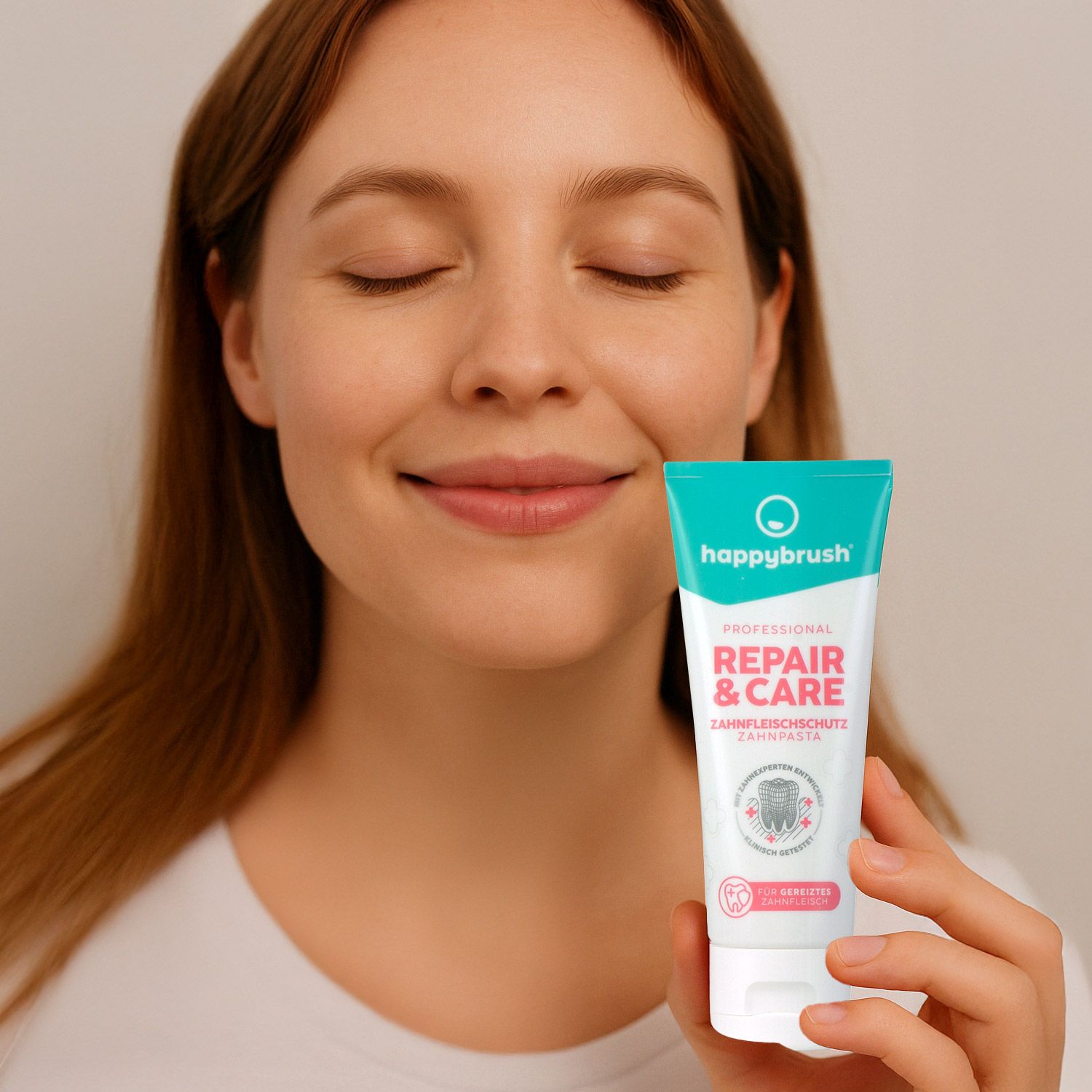 Frau hält Zahnpasta-Tube. Aufschrift: happybrush Repair & Care. Zahnfleischschutz. Frau lächelt mit geschlossenen Augen.