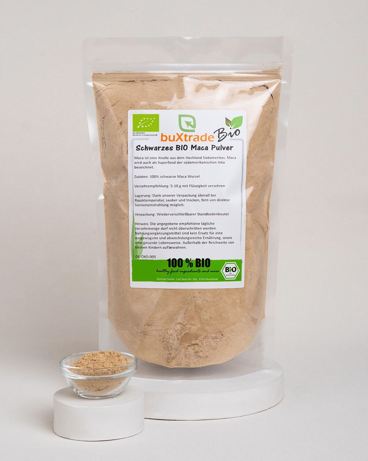 Schwarzes BIO Maca Pulver in einem Standbodenbeutel, daneben eine kleine Schale mit Pulver und ein Glas mit Getränk.