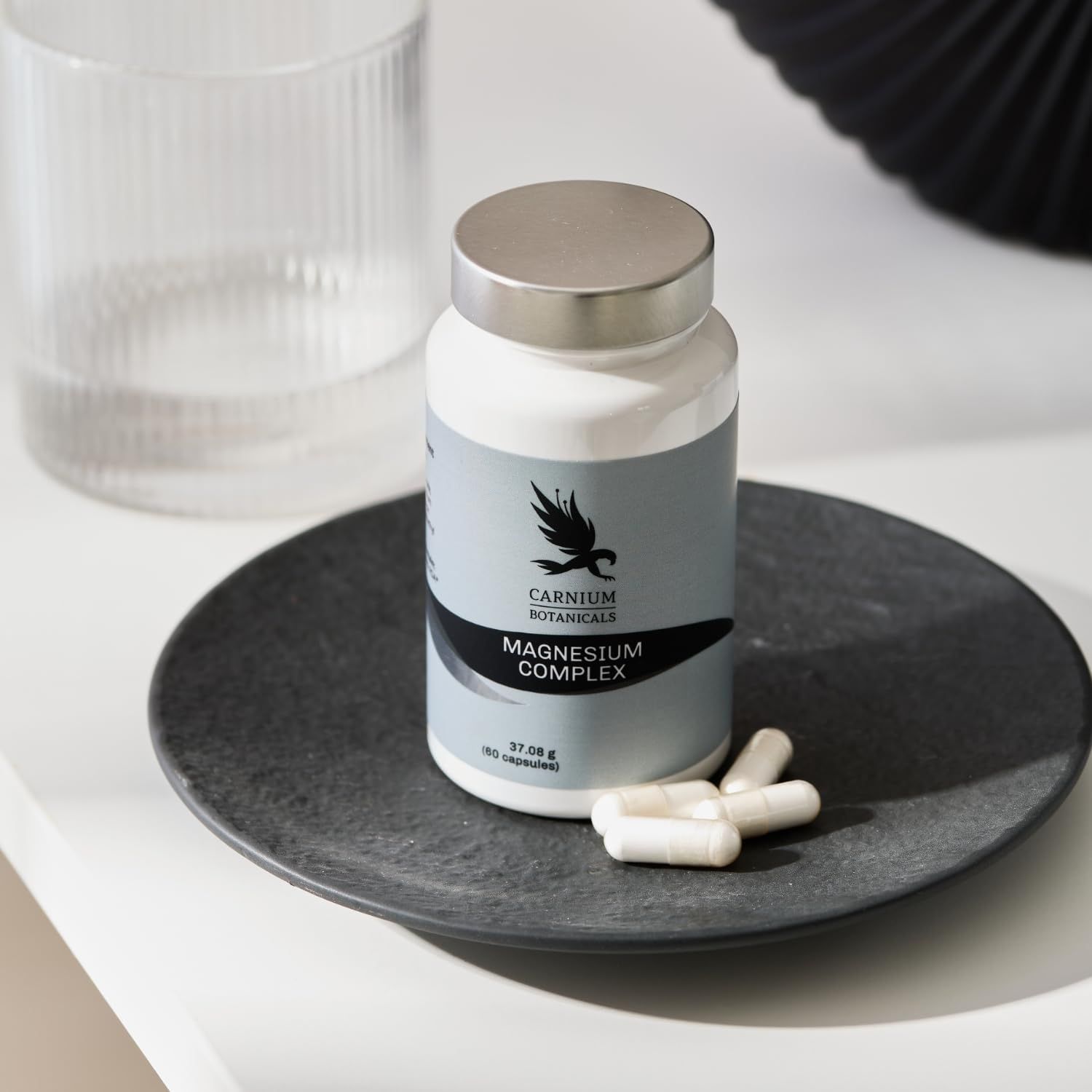 Weiße Flasche mit silbernem Deckel. Auf einem Teller liegen Kapseln. Aufschrift: CARNIUM BOTANICALS, Magnesium Complex.