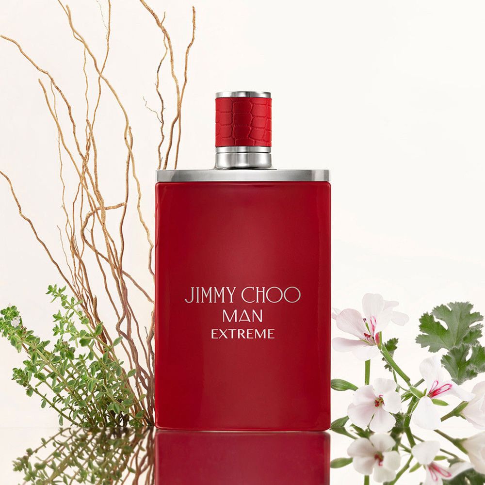 Roter Flakon mit silberner Kappe. Aufschrift: Jimmy Choo Man Extreme. Dekoriert mit Zweigen und Blumen.