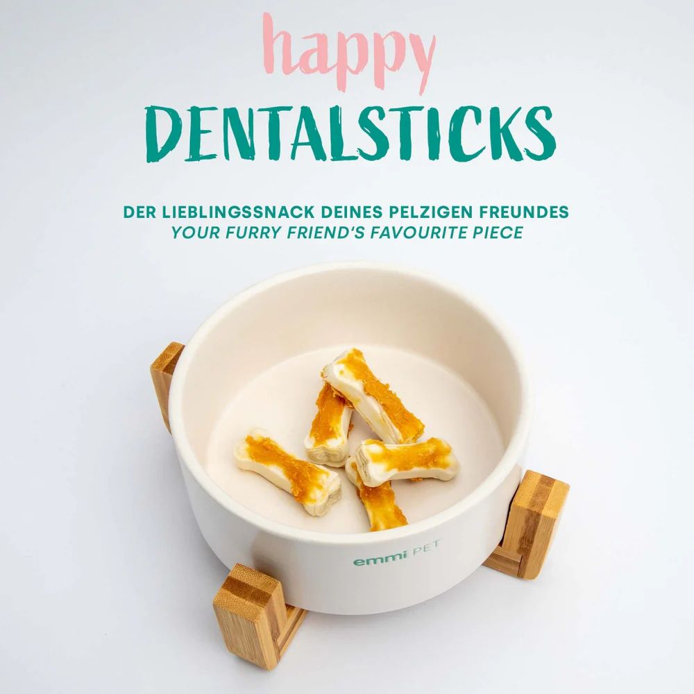 Weiße Schale mit "emmi-pet happy Dentalsticks". Die Sticks sind knochenförmig. Die Schale steht auf Holzfüßen.