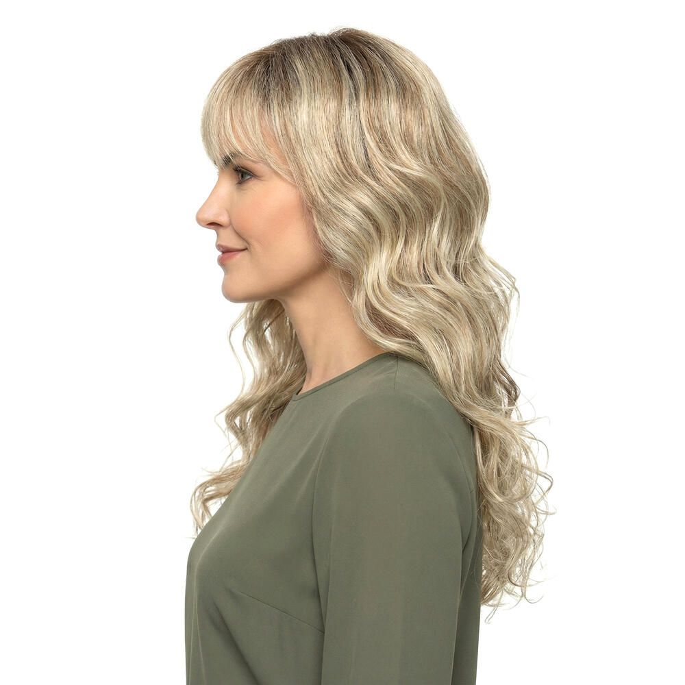 Blond gewellte Perücke mit Pony, Seitenansicht. Die Frau trägt ein grünes Oberteil. Hintergrund weiß.