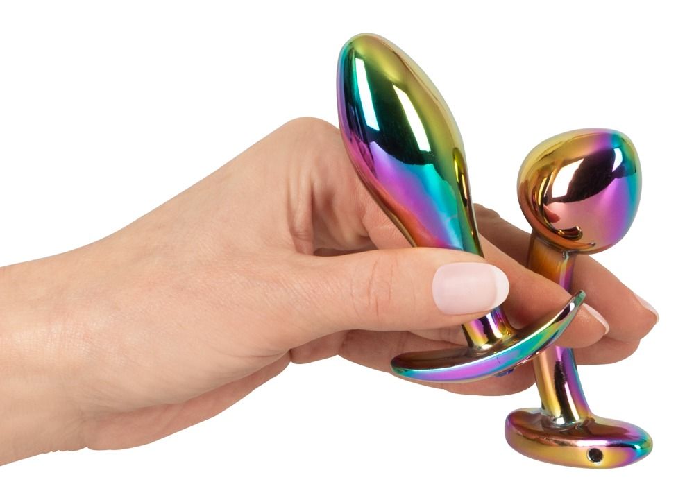 Hand hält zwei metallische Anal-Plugs mit Regenbogen-Finish.