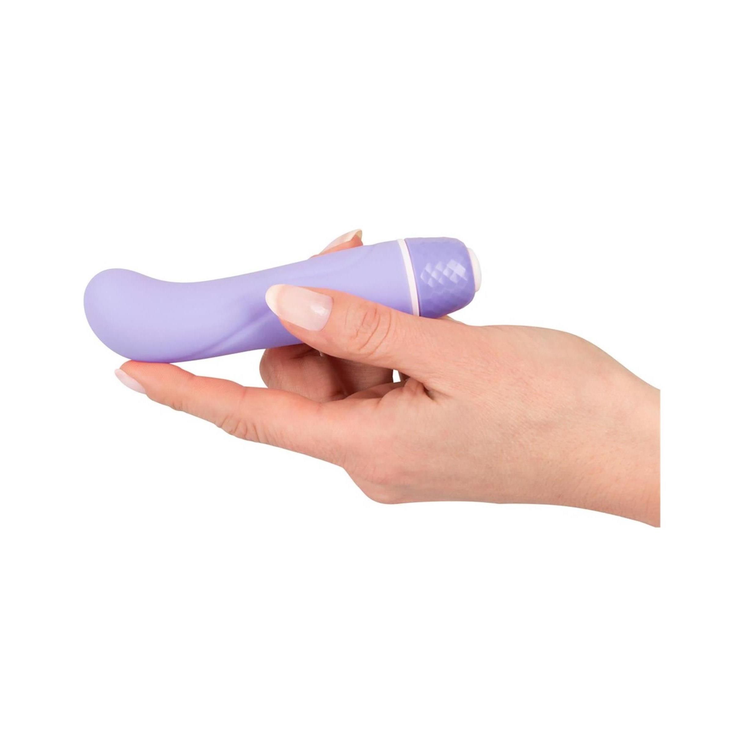Hand hält lila Vibrator. Gebogene Form, abgerundete Spitze. Wellenförmige Oberfläche. Weißer Sockel.