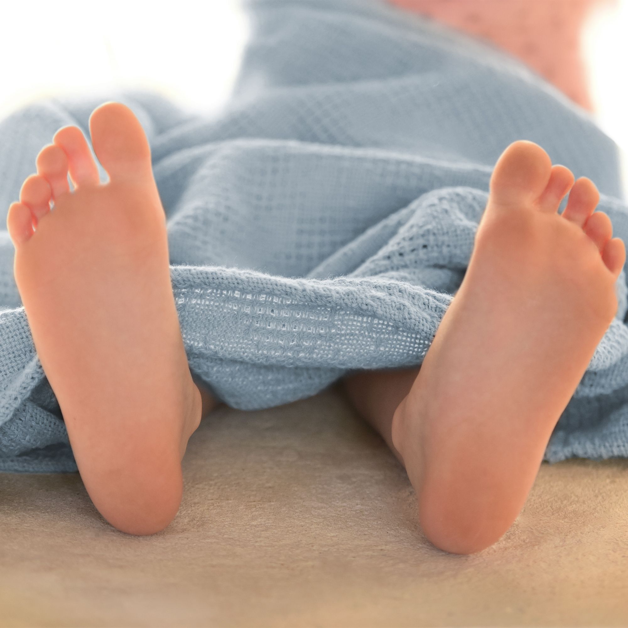 Babyfüße, teilweise von einer blauen Strickdecke bedeckt.