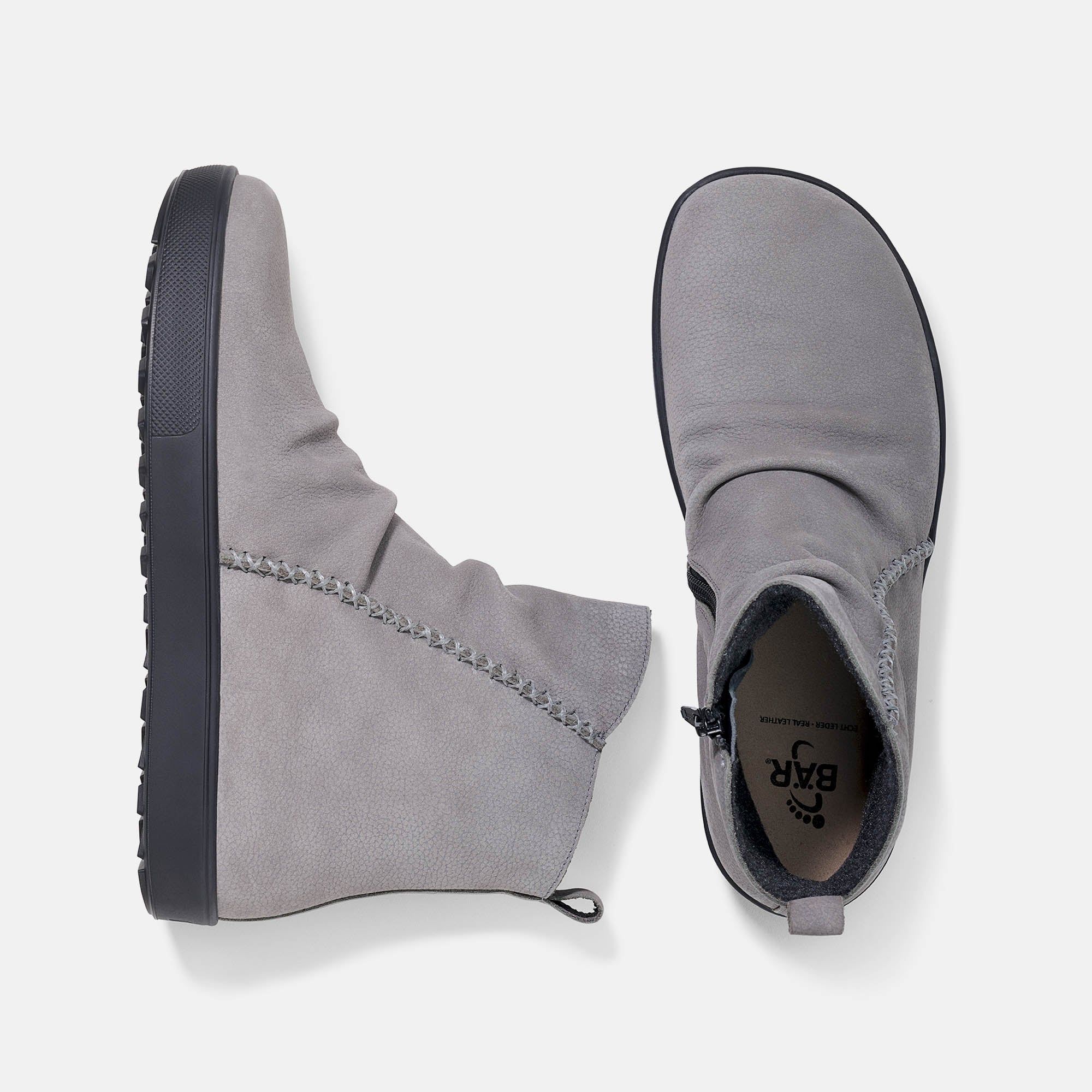 Zwei graue Stiefeletten mit schwarzer Sohle. Blick von oben. Innensohle mit Logo.