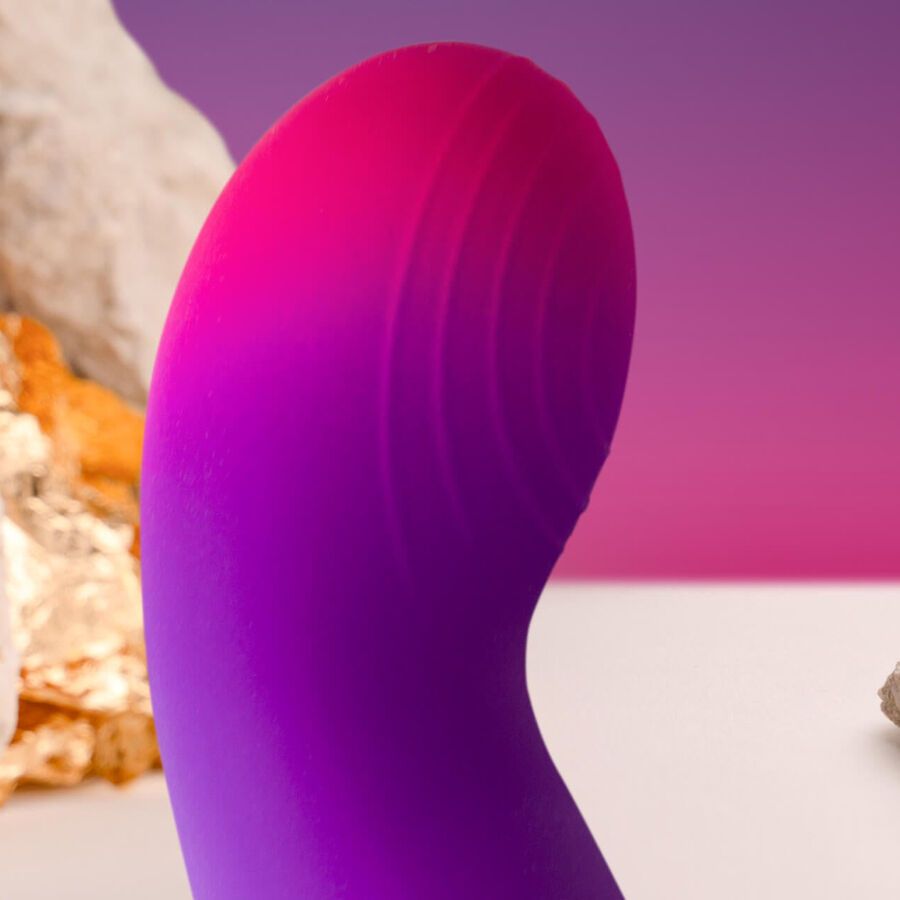 Lila-pinkfarbener Vibrator mit geschwungener Form. Nahaufnahme. Hintergrund mit Steinen.