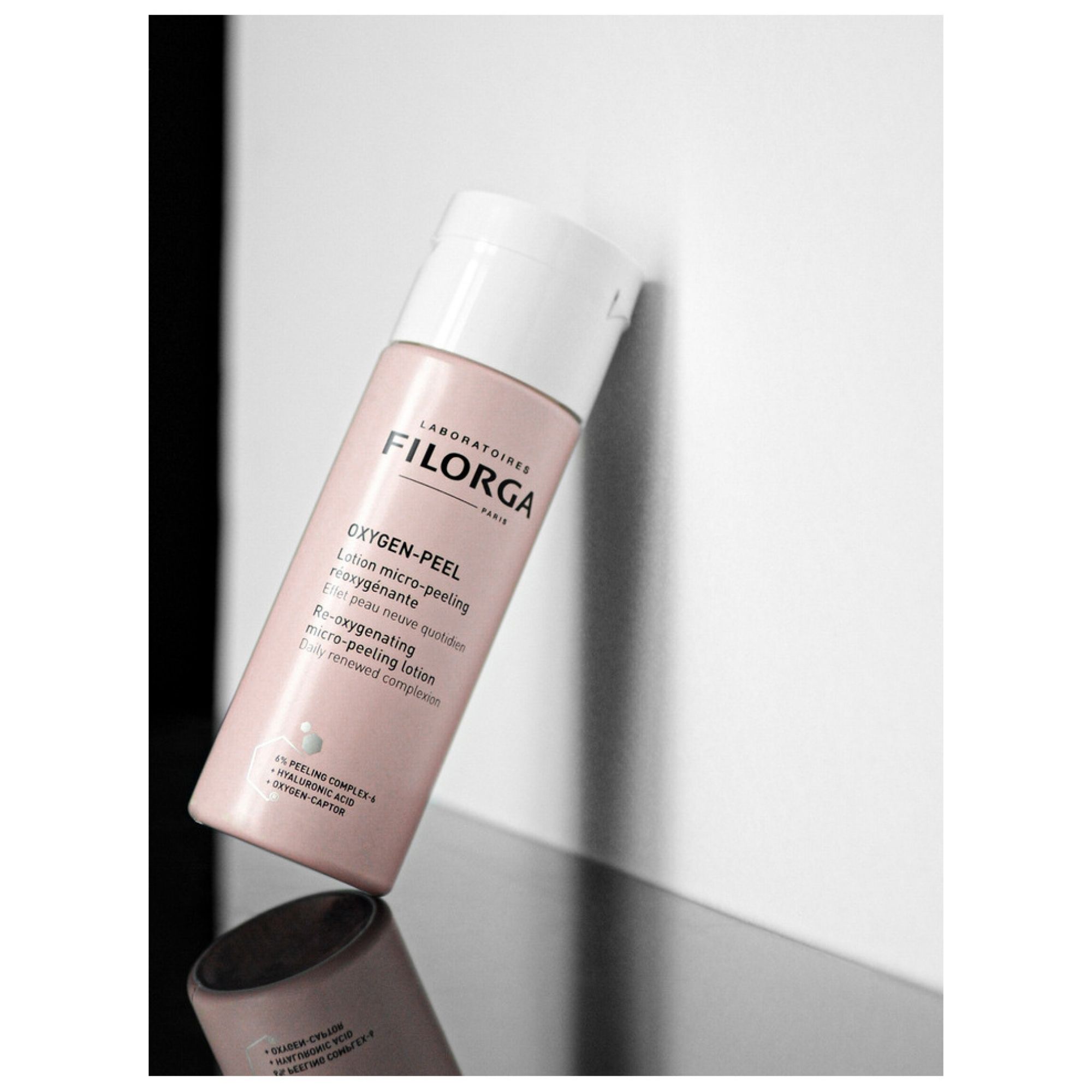 Filorga Oxygen-Peel Lotion micro-peeling réoxygénante in einer hellrosa Flasche, die auf einer spiegelnden Oberfläche lehnt.