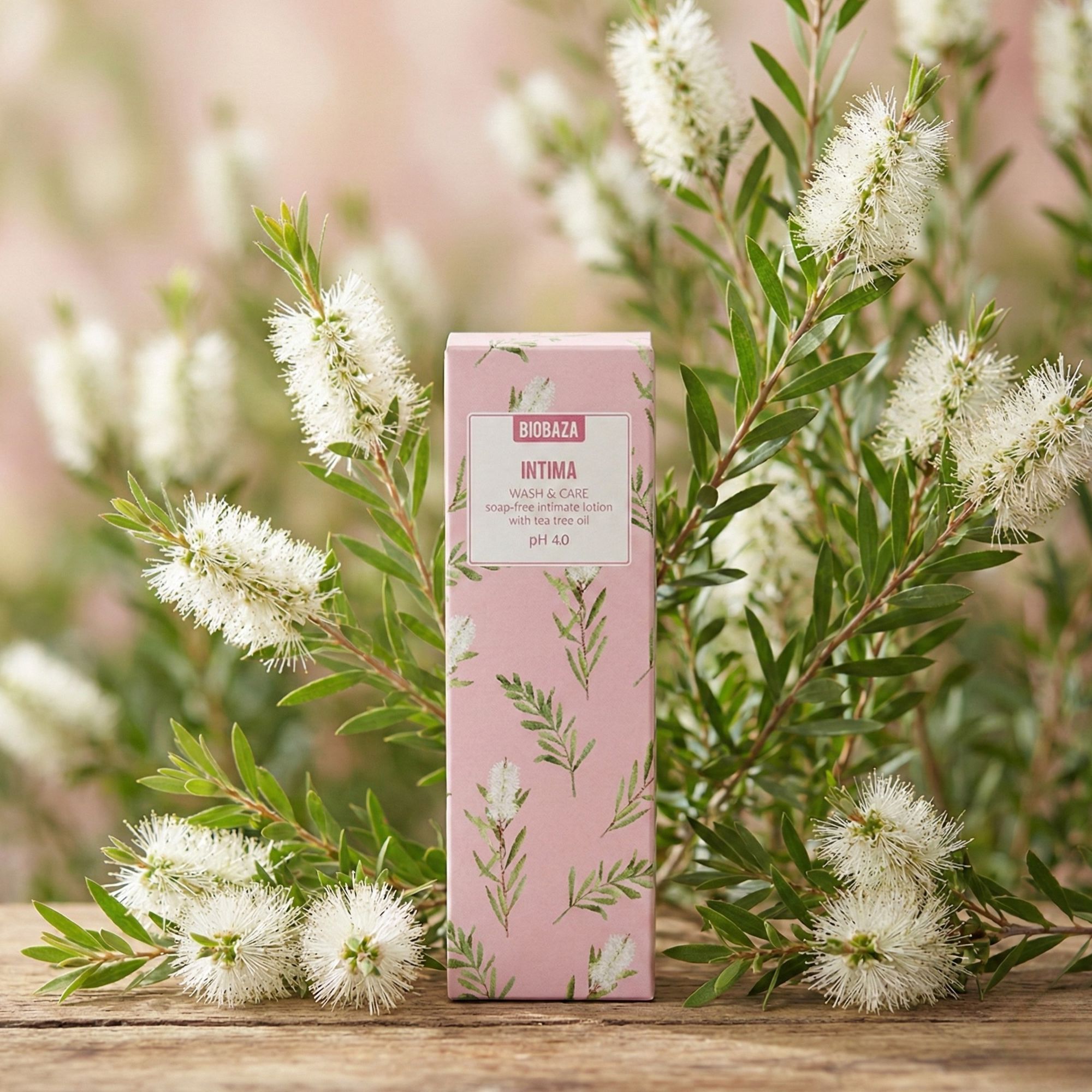Rosa Verpackung mit floralem Muster. Text: Intima Wash & Care, seifenfreie Intimwaschlotion mit Teebaumöl, pH 4.0. Umgeben von Zweigen mit weißen Blüten.