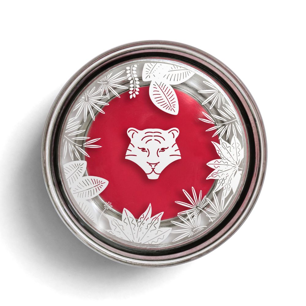 Runder Behälter mit rotem Inhalt. Silberner Rand mit Blättern und einem Tigerkopf. Deckel mit Logo.