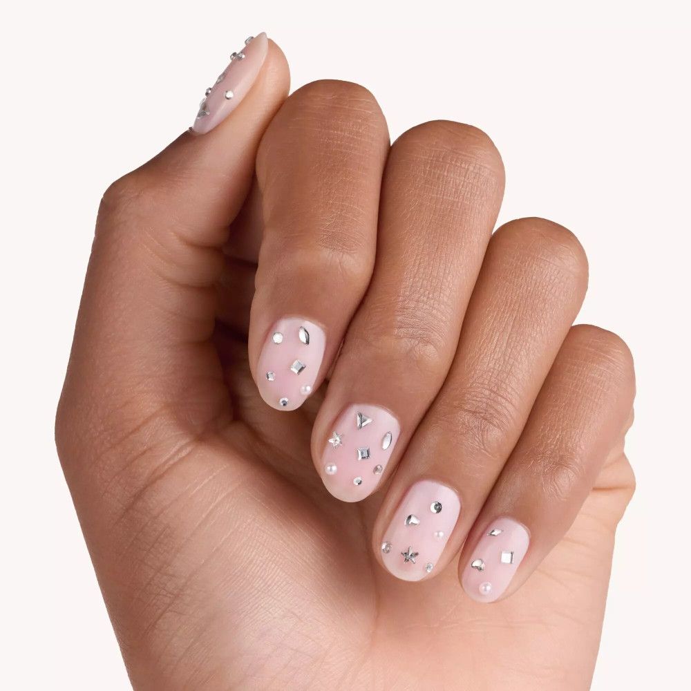 Hand mit lackierten Nägeln, verziert mit silbernen Nagelstickern in verschiedenen Formen. Helle Nagellackfarbe.