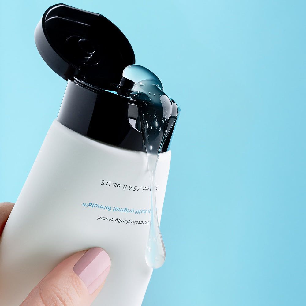 Hand drückt auf eine Tube, klares Gel fließt aus dem geöffneten Deckel.