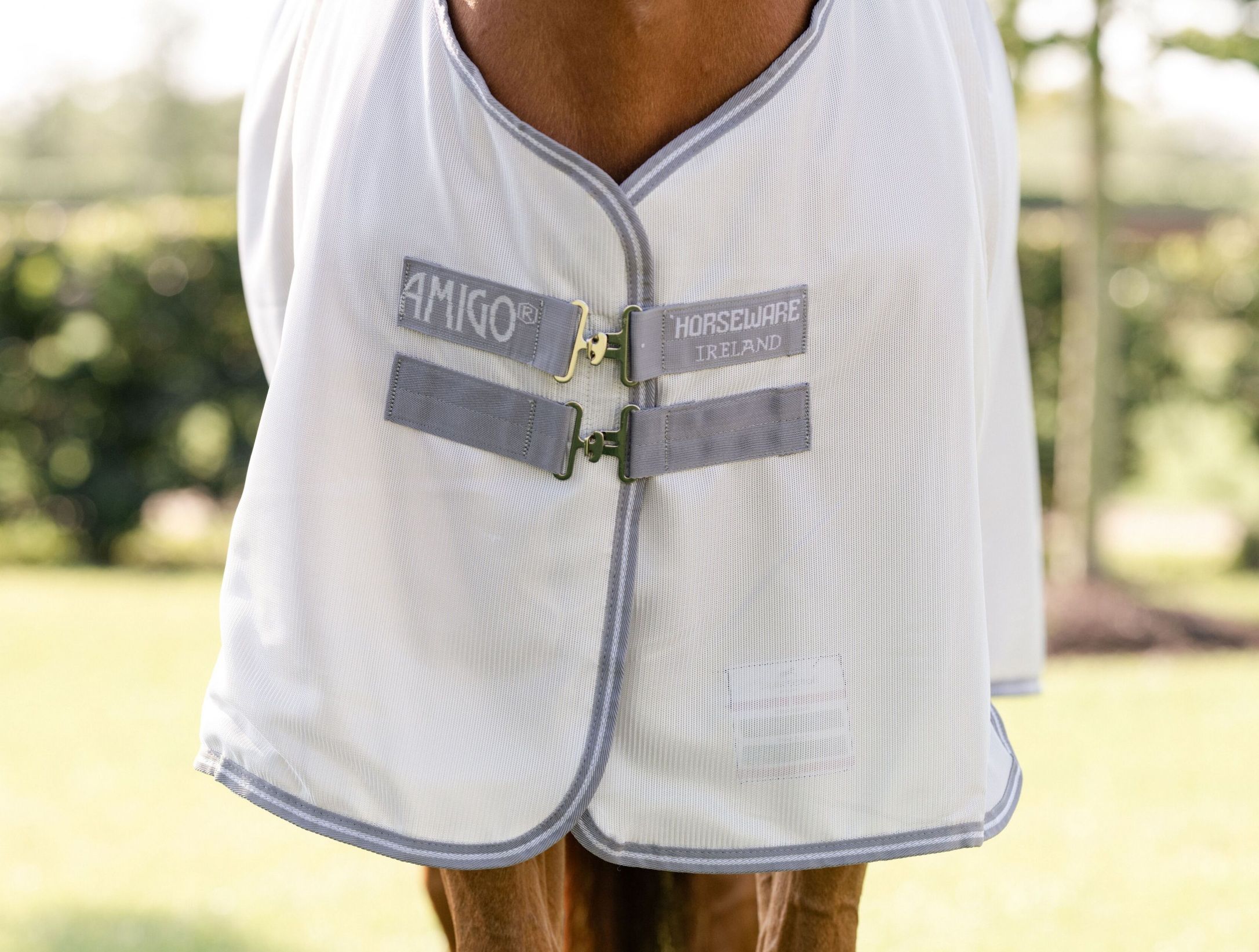 Nahaufnahme der Pferdedecke. Markenname AMIGO und HORSEWARE IRELAND. Graue Riemen mit Schnallen.