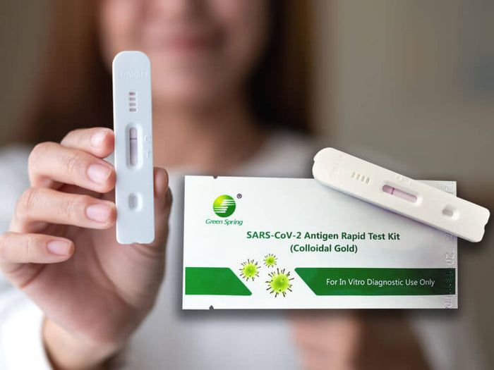 Person hält einen weißen SARS-CoV-2 Antigen Schnelltest und eine Packung. Aufschrift: Green Spring, SARS-CoV-2 Antigen Rapid Test Kit.