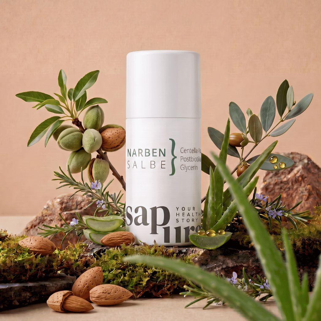 Weiße Pumpspender-Flasche 'Narbensalbe' umgeben von Aloe Vera, Mandeln und Kräutern.