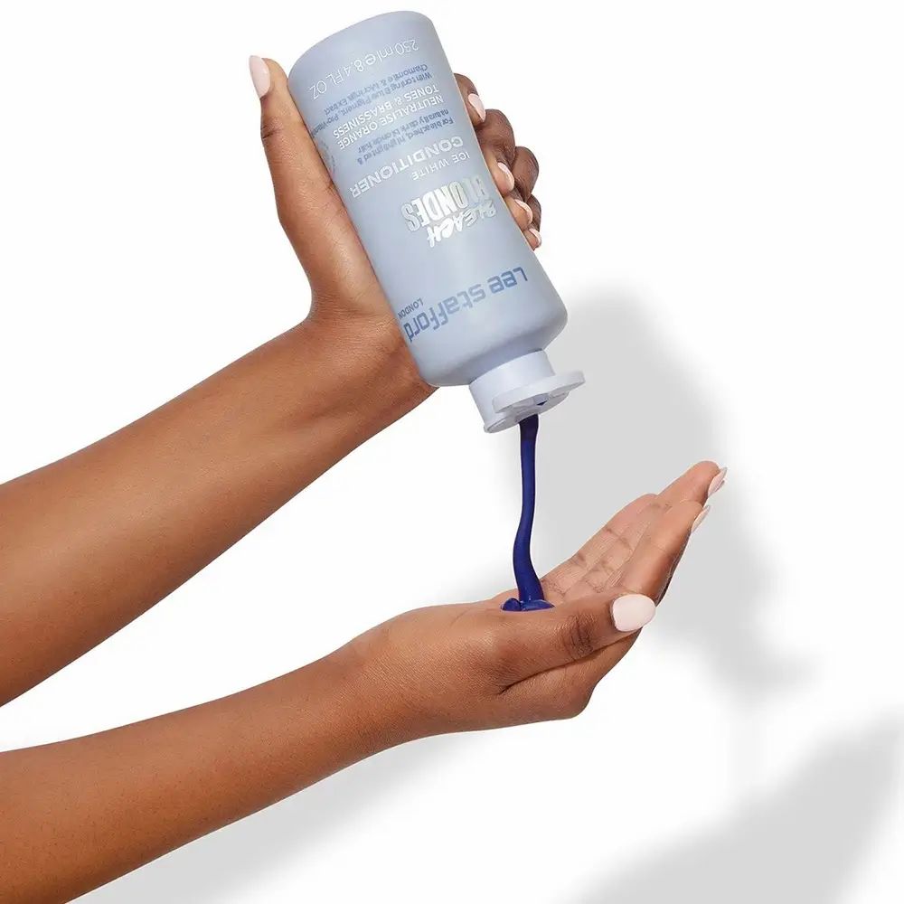 Hände halten eine hellblaue Flasche. Produkt wird in die Handfläche gegossen. Produkt: LEE STAFFORD Bleach Blondes Conditioner.