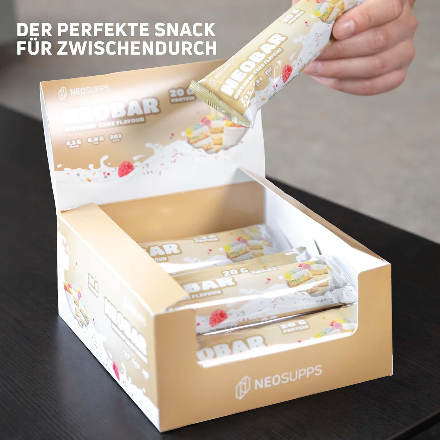 Eine Hand nimmt einen Neosupps NeoBar Birthday Cake Proteinriegel aus einer geöffneten Box.